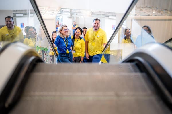 Un gruppo di dipendenti IKEA con le loro uniformi gialle e blu è in piedi in un ambiente luminoso e moderno, vicino a una scala mobile.