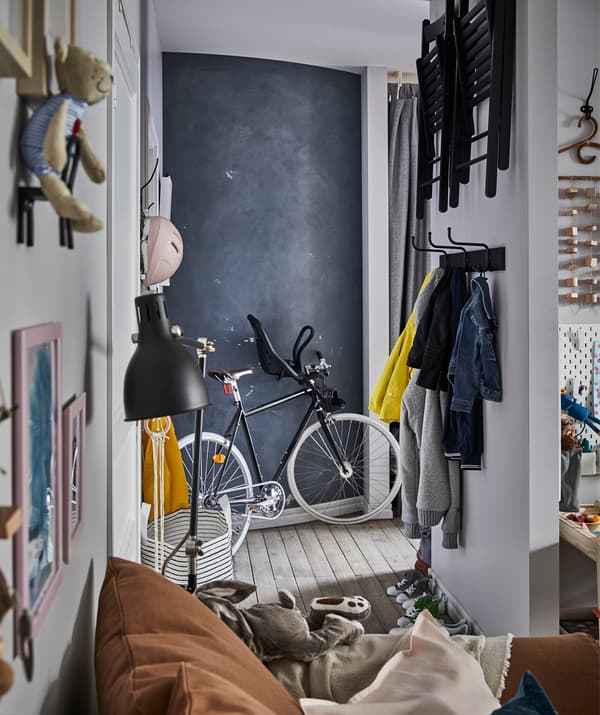 Un hall d’entrée avec des vêtements et des chaises pliantes rangées sur le mur, un vélo et un mur tableau noir.