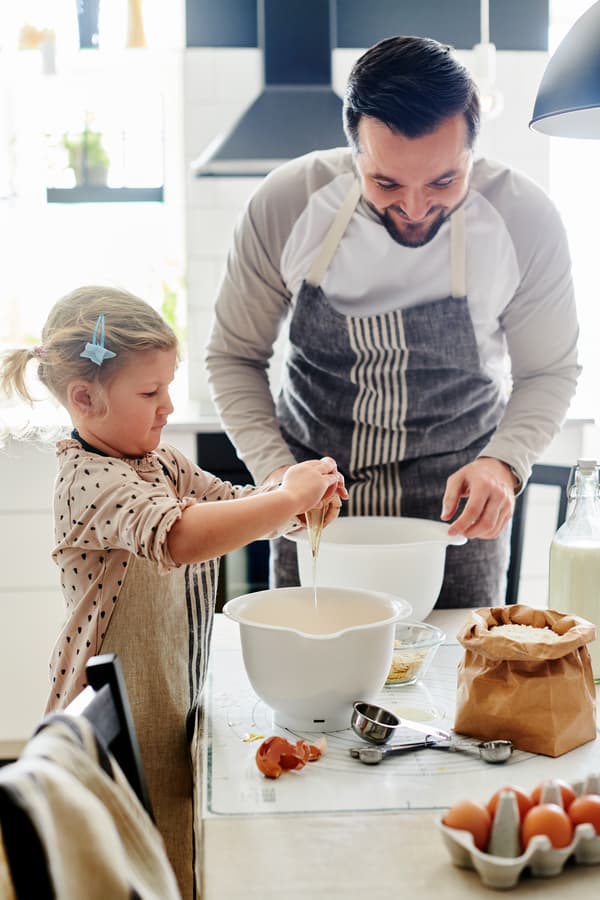Un hombre con su hija cocinando. Sobre la cubierta de cocina hay dos bowls de cocina blancos IKEA, huevos y otros utencilios de cocina.