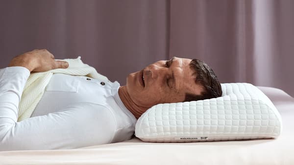 Un homme couché sur le dos, la tête posée sur un oreiller haut.