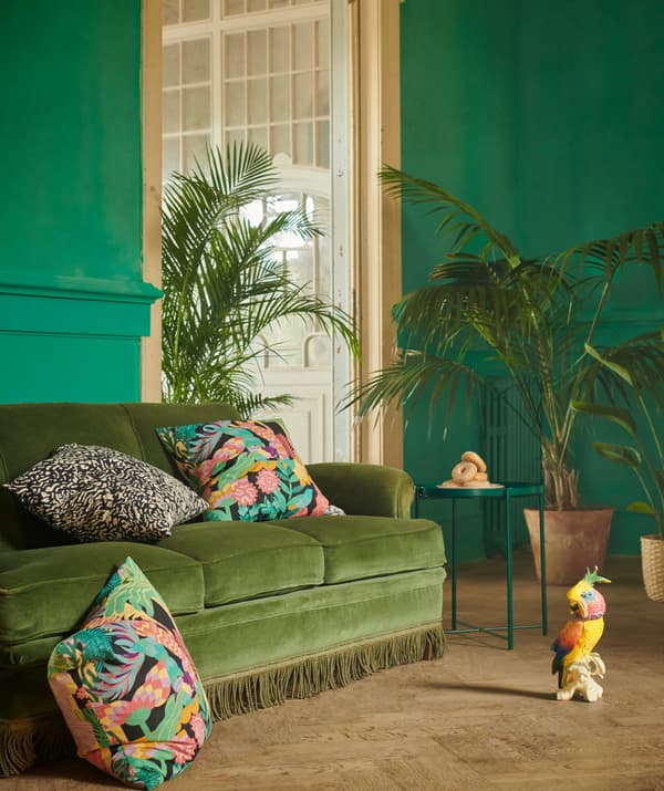 Un intérieur dans un style élégant aux tons verts. De grandes plantes près d’un canapé avec des coussins GRIMHILD et NÄBBFLY.