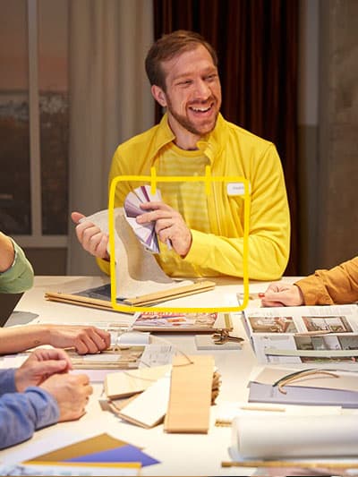 Un Interior Designer IKEA conseille un groupe de client-e-s autour d’une table à l’aide de prospectus, croquis et cartes de couleur