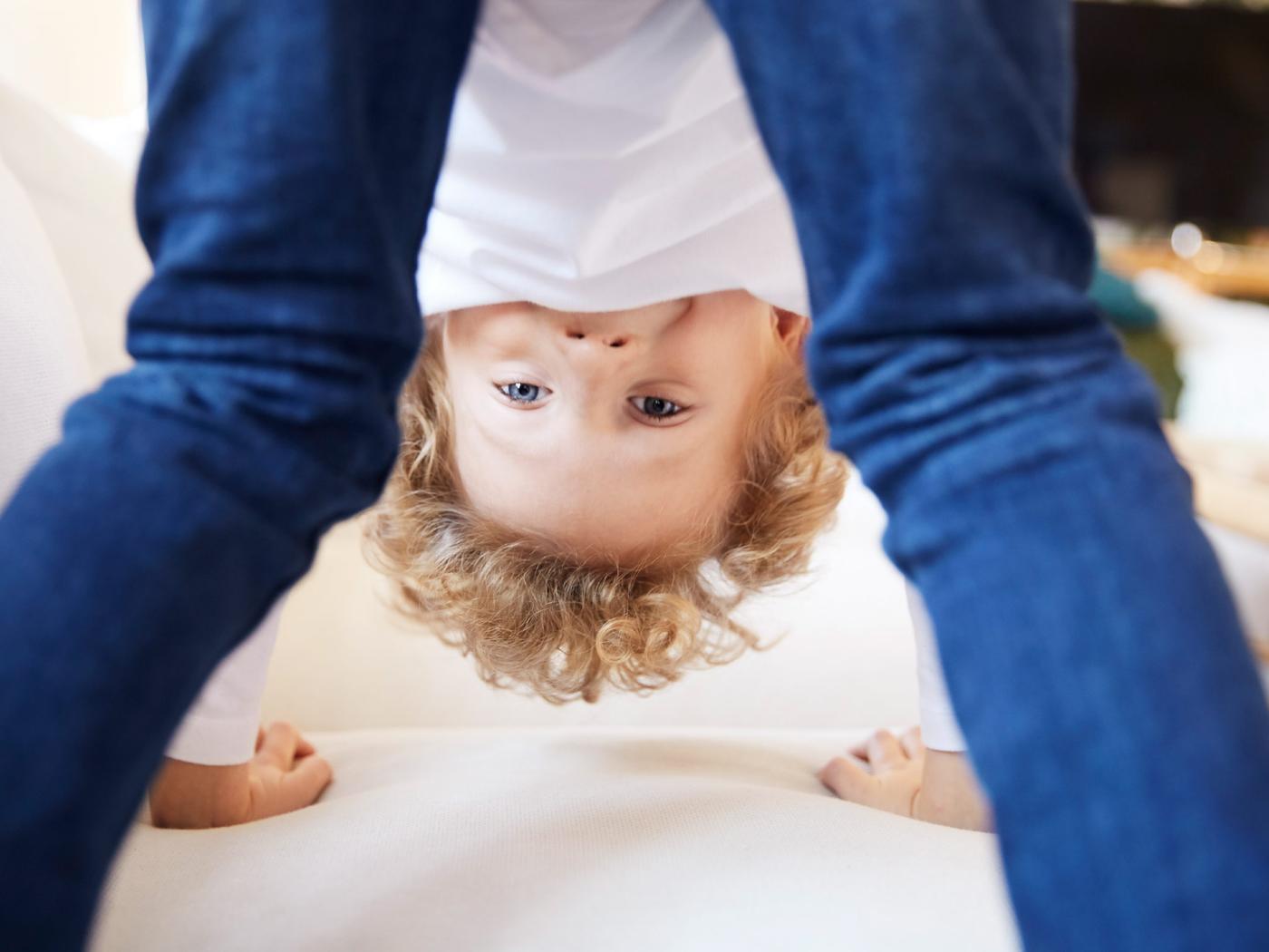 Un jeune garçon s’amuse: les mains sur le sol et la tête entre les jambes, il regarde l’objectif.