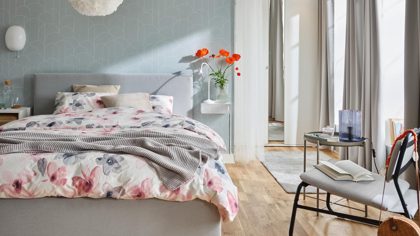 Un letto GLADSTAD in una camera grigia con biancheria da letto LAPPNYCKLAR dal motivo floreale. Accanto, una poltrona e un tavolino - IKEA