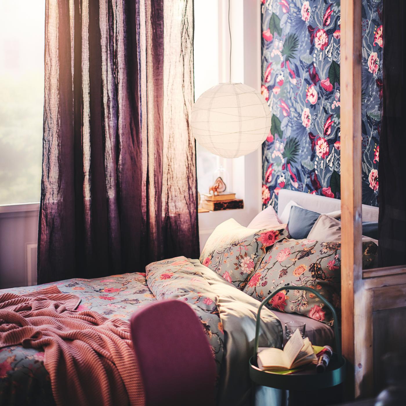 Un lit avec un jeté et un ensemble housse de couette et taie d’oreiller NÄSSELKLOCKA, avec un abat-jour suspension au-dessus.