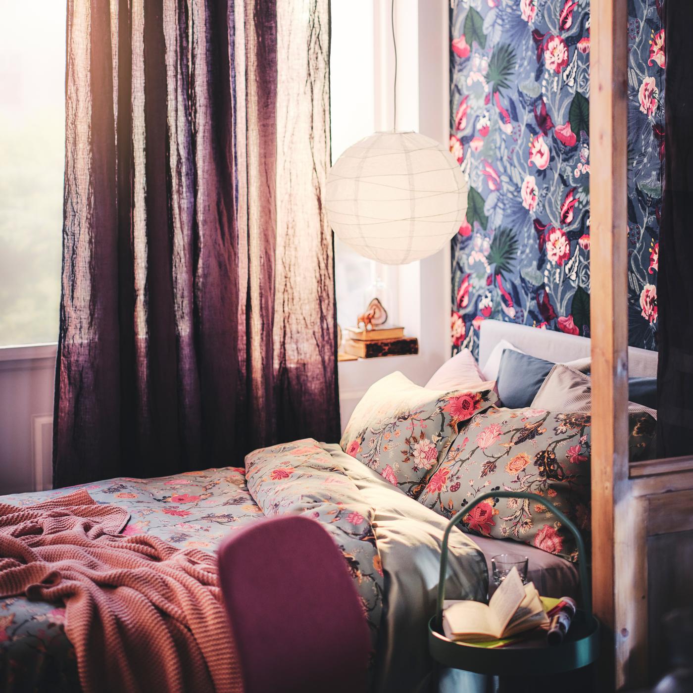 Un lit avec un plaid et du linge de lit en ensemble housse de couette et taie NÄSSELKLOCKA, sous un abat-jour suspension.