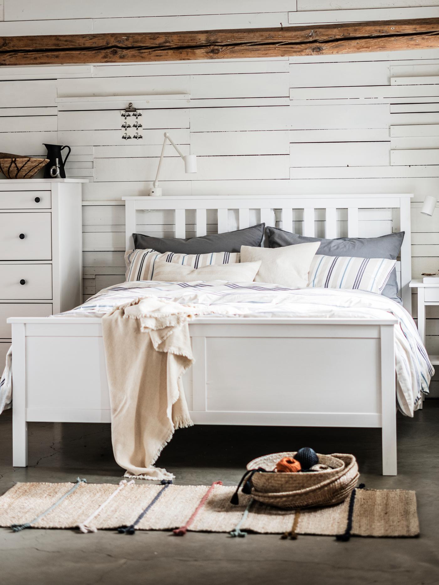 Un lit double HEMNES dans une chambre à coucher, contre un mur, à côté d’une commode 6 tiroirs HEMNES.