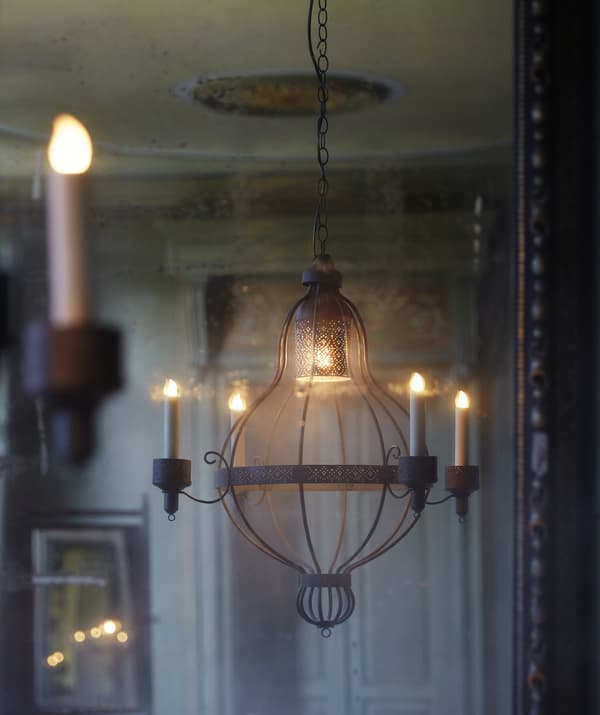 Un lustre à quatre branches suspendu dans une pièce aux tons crème, avec une porte ornée à l'arrière-plan.
