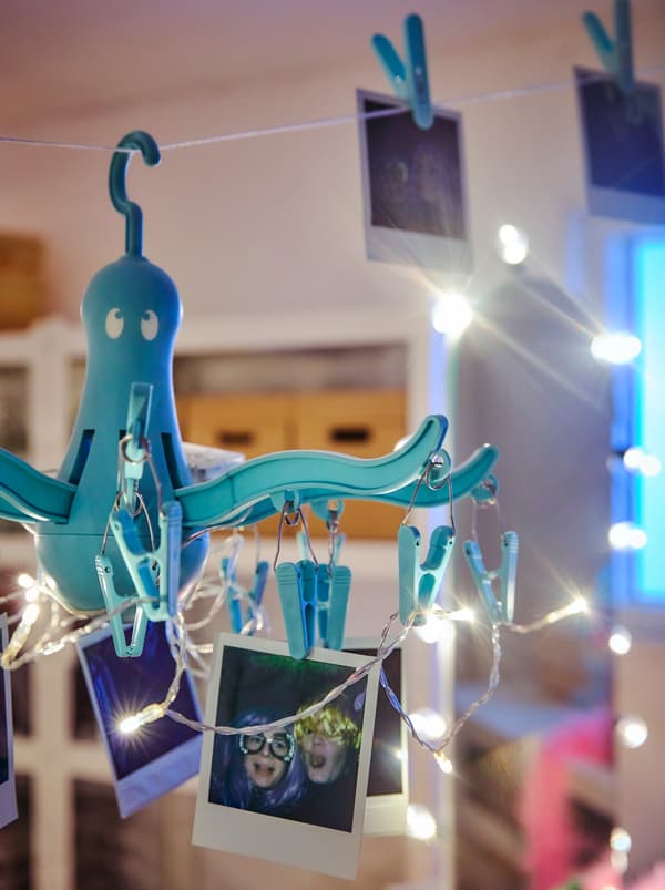 Un lustre improvisé avec un séchoir à suspendre PRESSA et une guirlande lumineuse LEDFYR; des polaroïds sont accrochés aux pinces à linge.