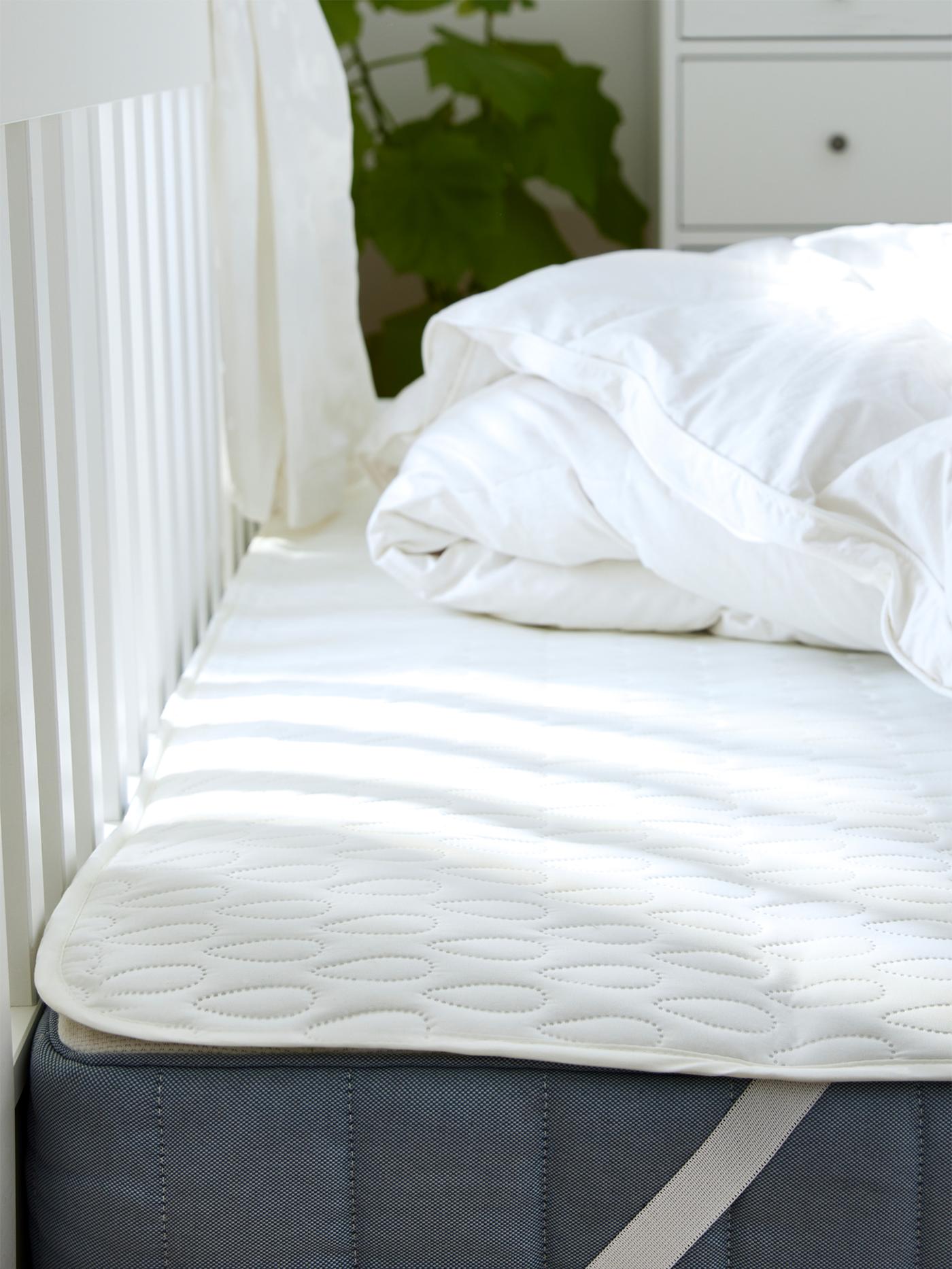 Un matelas recouvert d’une alèse posé sur un cadre de lit. Une couette froissée repose sur l’alèse.