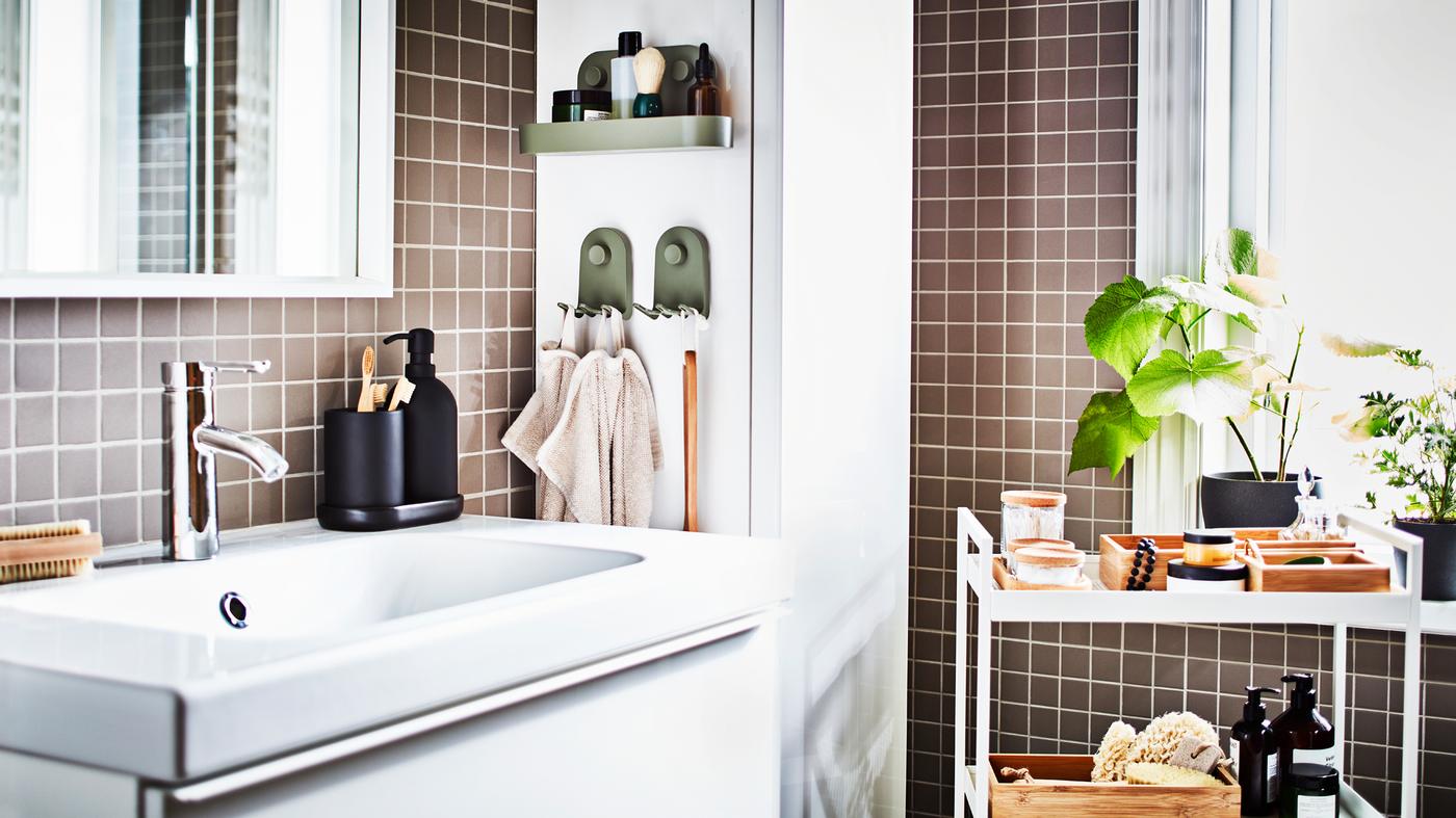 Un meuble lavabo blanc, un miroir blanc, une desserte blanche avec des plateaux et des bocaux et un meuble colonne blanc dans une salle de bain à carrelage gris.