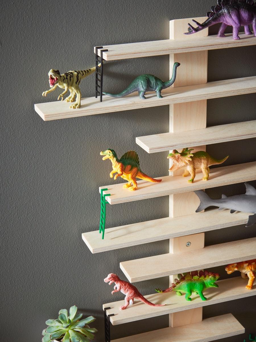 Un mueble con siete repisas de madera. En cada repisa hay juguetes de dinosaurios de direrentes colores.