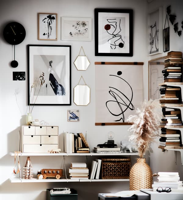 Un mur décoratif avec cadres, boîtes, livres, horloge, jouets et vase ; le tout dans des tons blancs, noirs et brunâtres.