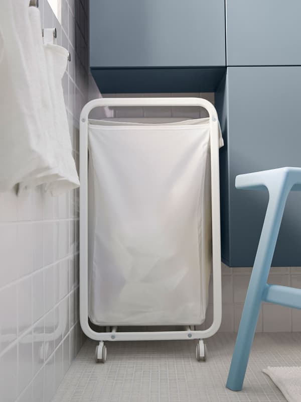 Un panier à linge blanc encastré dans l’espace entre l’armoire et le mur dans une petite salle de bain.