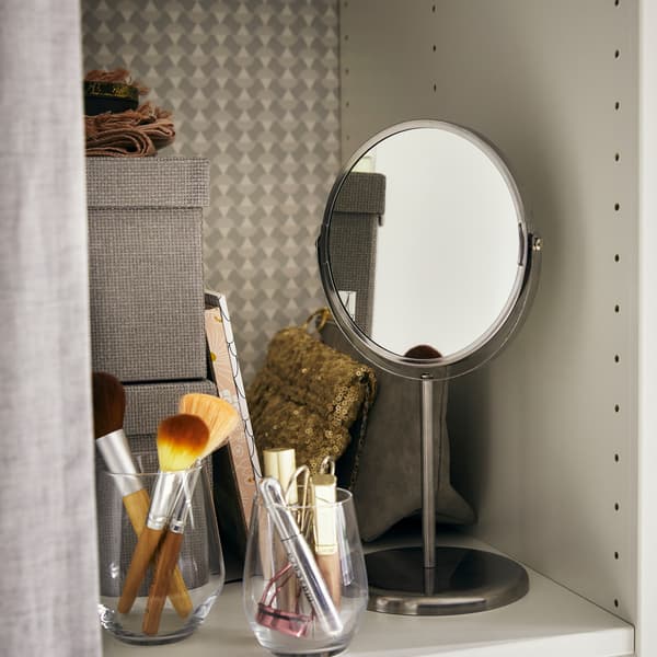 Un petit miroir et des pots pour les pinceaux de maquillage disposés sur une tablette avec des boîtes de rangement.