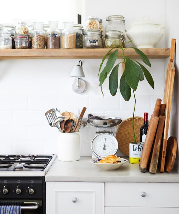 Un plan de travail avec une cuisinière et des planches en bois, et des bocaux remplis d'ingrédients secs disposés sur une tablette en bois au-dessus.