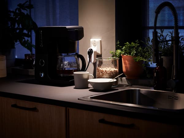 Un plan de travail de cuisine avec une cafetière reliée à une prise connectée – une tasse et un bol à côté d’un évier.