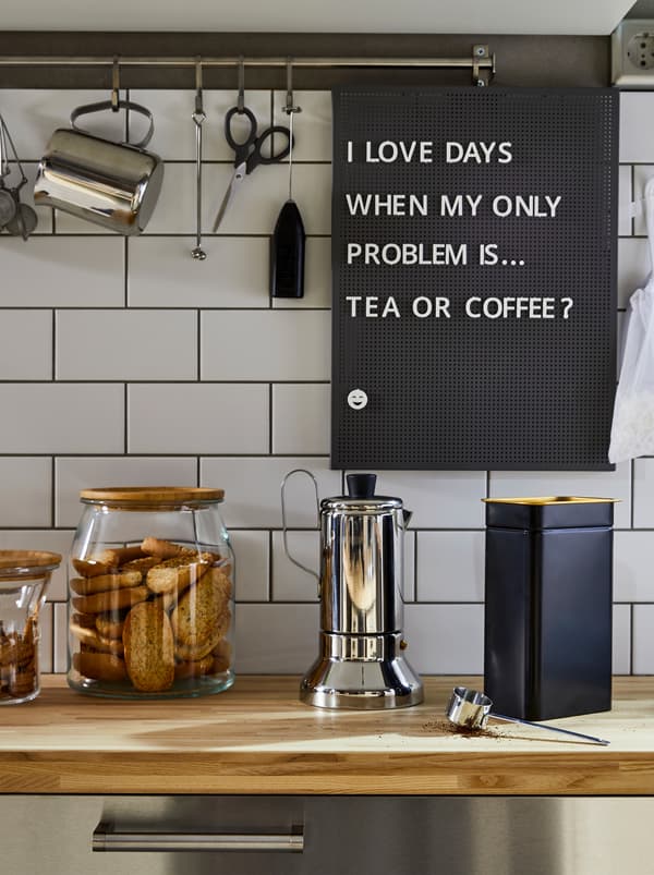 Un plan de travail de cuisine avec une machine à expresso METALLISK en acier inoxydable, une boîte à café BLOMNING bleue et des récipients en verre pour les biscuits.