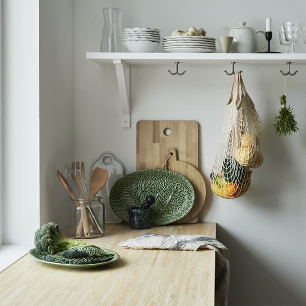 Un plan de travail de cuisine en bois avec une assiette en forme de feuille, des planches à découper en bois et de la vaisselle sur une étagère.