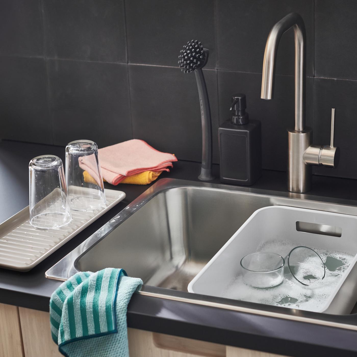 Un plan de travail EKBACKEN anthracite avec un évier contenant une bassine GRUNDVATTNET grise, plus des chiffons en microfibres.