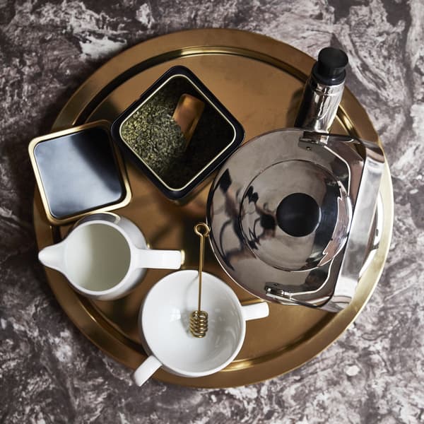 Un plateau rond en or avec bouilloire, tasse, pot à lait et thé en vrac dans un récipient.