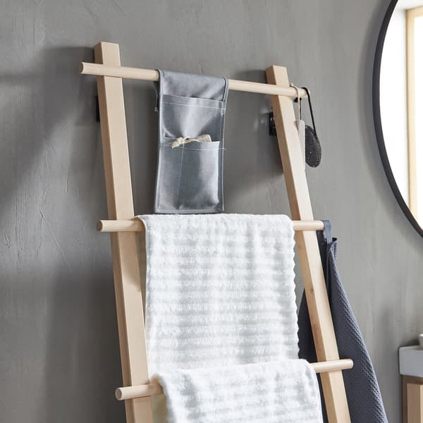 Un portant à serviettes VILTO style échelle en bouleau appuyé sur le mur gris d’une salle de bain minimaliste.