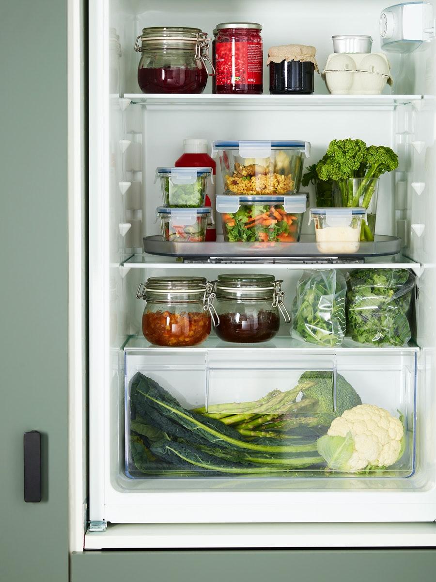 Un refrigerador con recipientes de plástico y vidrio SVALNA con alimentos como frutas y verduras en su interior. 