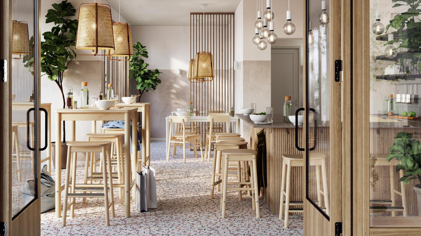 Un restaurant aéré avec des tables et des tabourets en bouleau RÖNNINGE bien rangés sous des suspensions en bambou KNIXHULT.