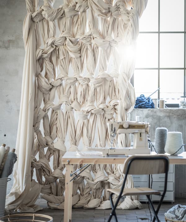 Un rideau fabriqué avec du tissu tricoté est suspendu derrière une table sur laquelle se trouve une machine à coudre.