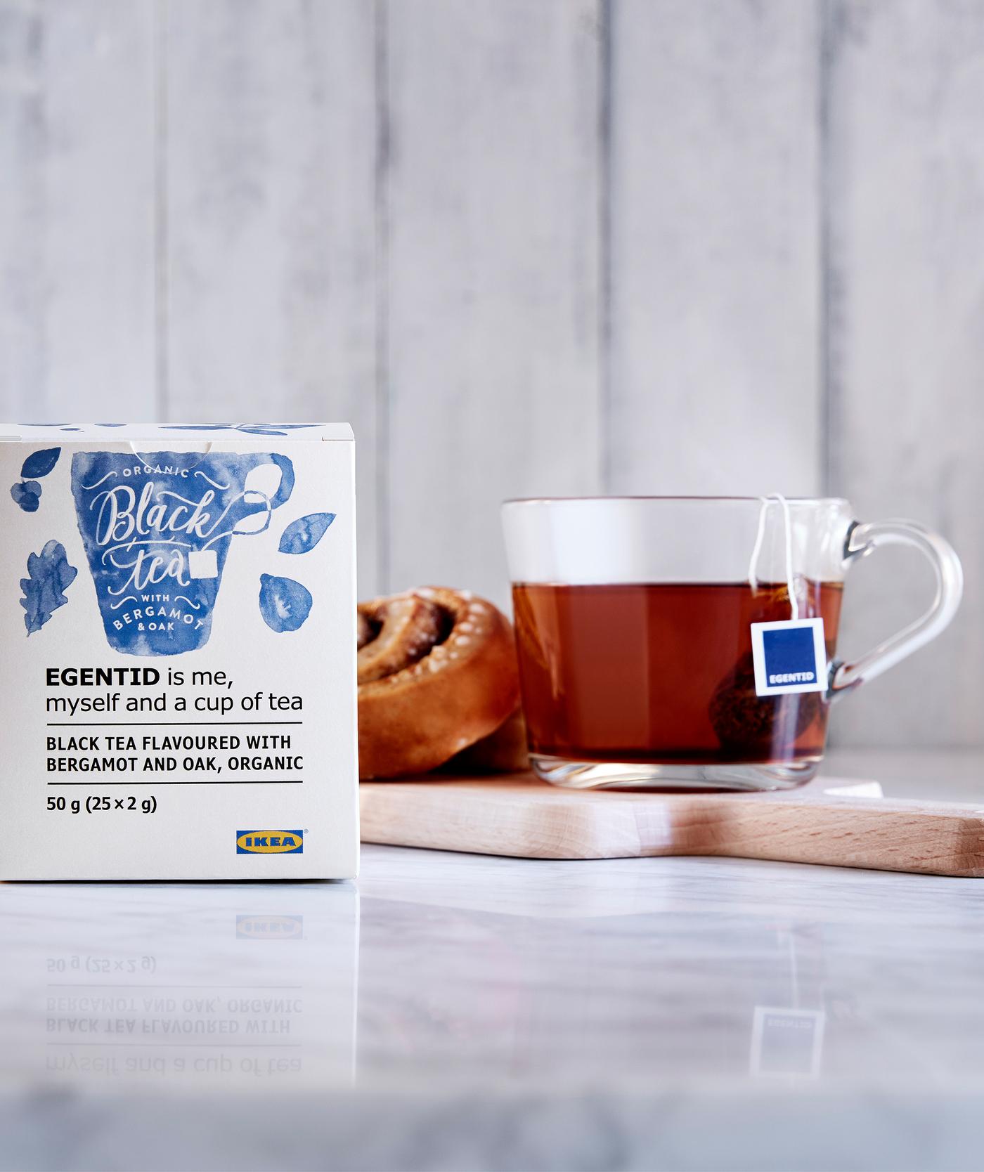 Un roulé à la cannelle et une tasse de thé sur un petit plateau, posé sur un plan de travail en marbre, un sachet de thé sur le côté.