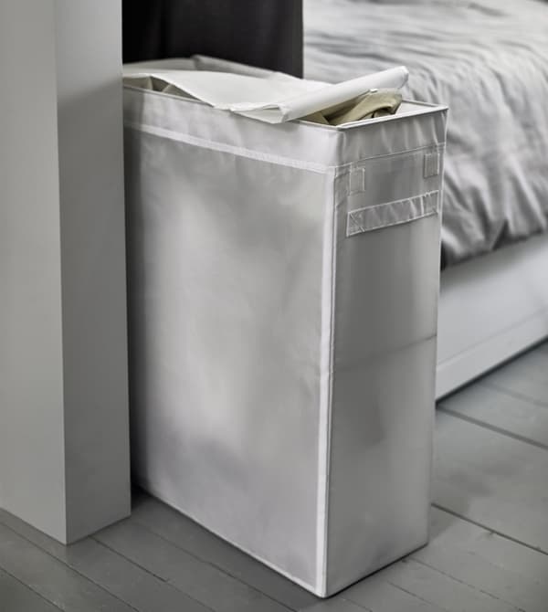 Un sac à linge blanc étroit est installé au pied du lit.