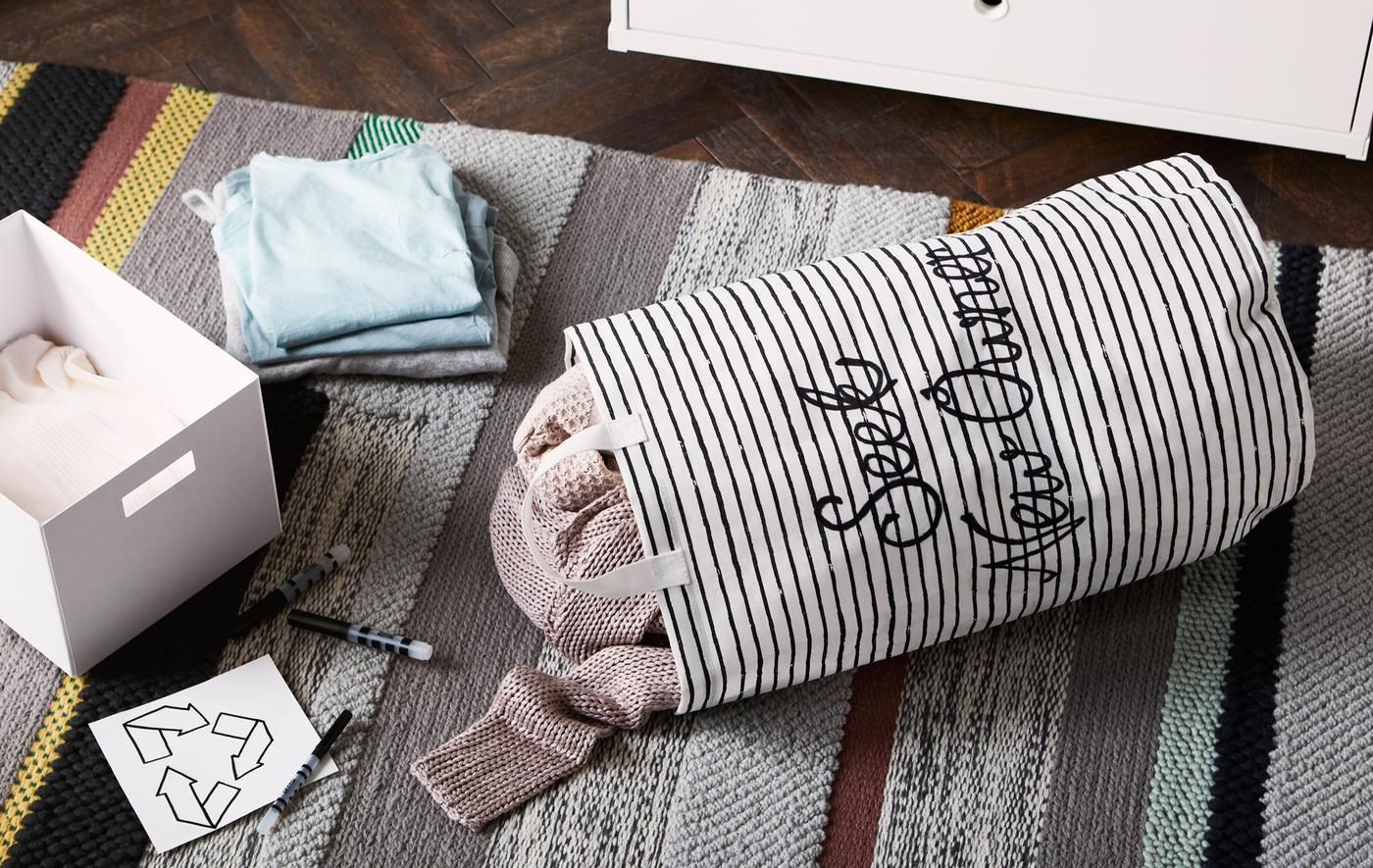 Un sac rayé noir et blanc et une boîte blanche sur un tapis rayé, avec un symbole de recyclage dessiné sur un bout de papier.