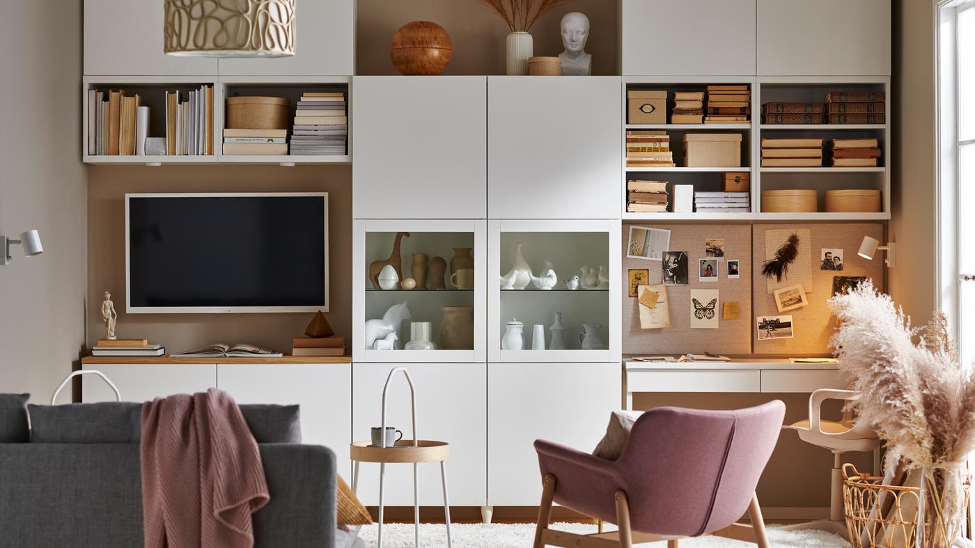 Un salon avec un rangement modulaire BESTÅ blanc couvrant un mur, des rangements ouverts et fermés, un canapé, une télévision et un poste de travail.