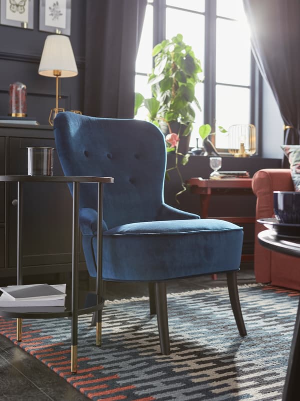Un salon ensoleillé avec un fauteuil REMSTA bleu sur un tapis à motifs RESENSTAD coloré.