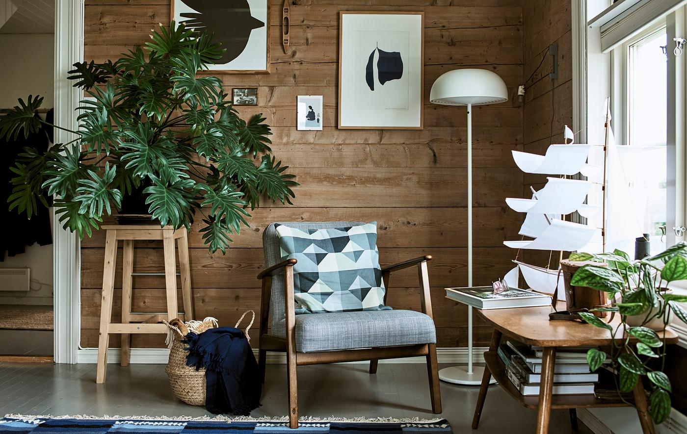 Un salon rustique avec un fauteuil à structure en bois, un lampadaire blanc et un tabouret utilisé comme piédestal pour une plante à grandes feuilles.