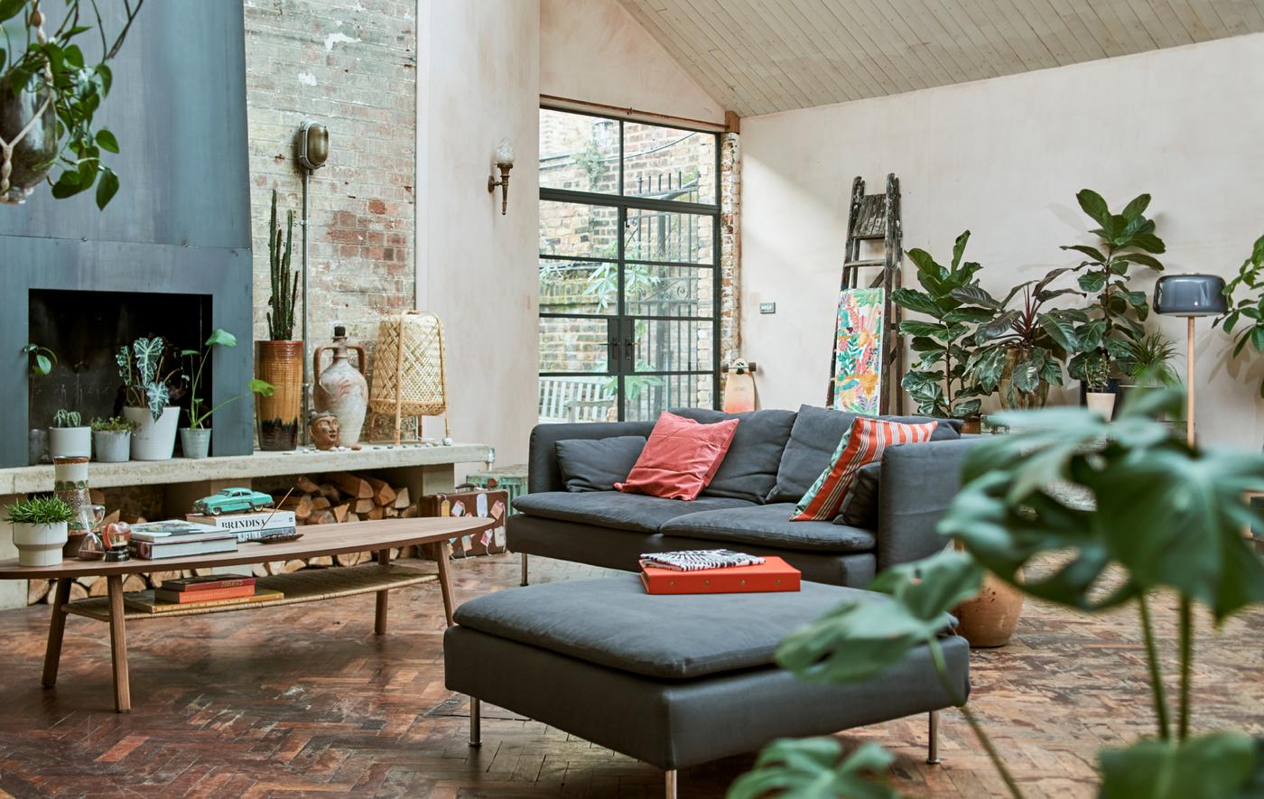 Un séjour de style entrepôt avec des murs de briques, un feu ouvert, un sol en parquet, un canapé et un repose-pieds bleus, une table basse et des plantes vertes.