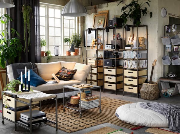 Un séjour décontracté et éclectique avec des plantes, de grandes fenêtres et des meubles de rangement en bois et en métal de style industriel.
