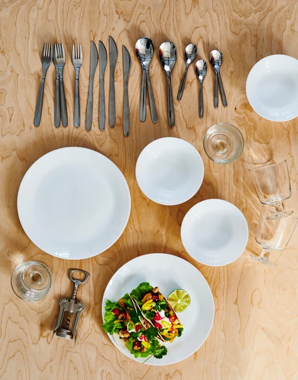 Un service de table sur du bois clair: assiettes et bols OFTAST blancs, couverts MOPSIG, verres à vin et ouvre-bouteille.