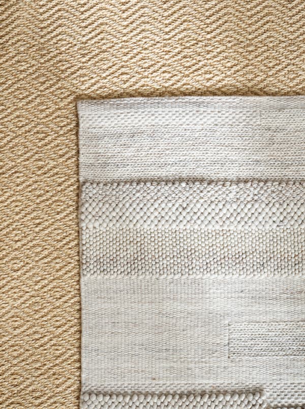 Un tapis BRÖNDEN posé de façon symétrique sur le dessus d’un tapis VISTOFT, les deux tapis ayant des couleurs et des textures naturelles.