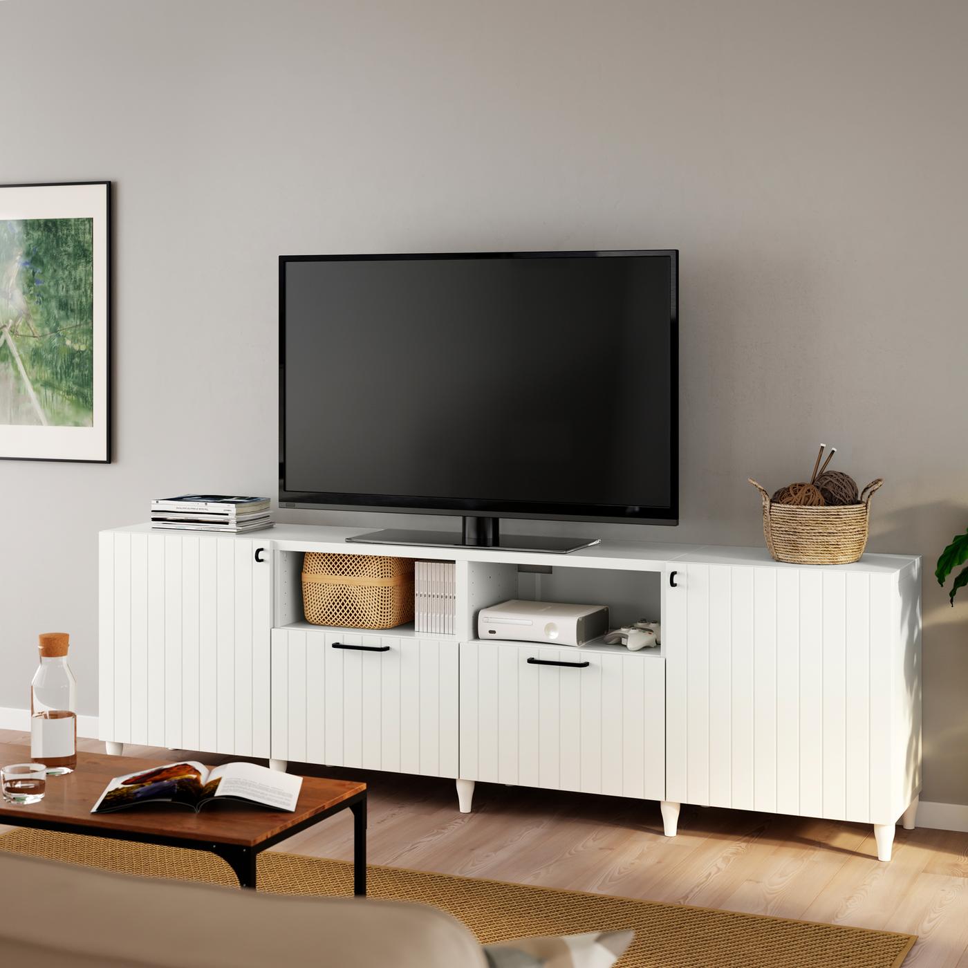 Un téléviseur noir sur un meuble télé BESTÅ blanc avec des pieds KABBARP blancs et des façades de portes/tiroirs SUTTERVIKEN blanches.