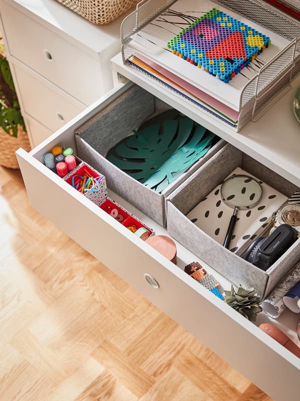 Un tiroir du haut d’une commode ouvert révèle du papier et des accessoires de dessin rangés dans des boîtes KOMPLEMENT.