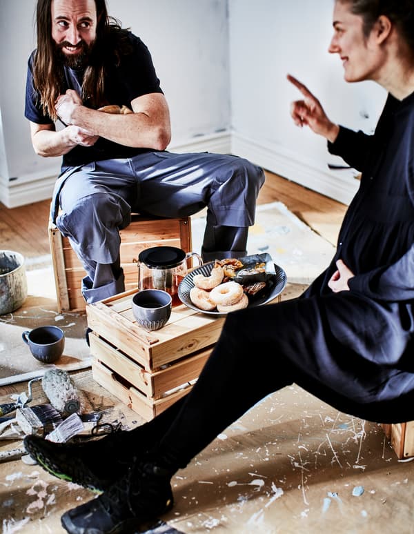 Un uomo e una donna scherzano durante una pausa caffè improvvisata, organizzata appoggiandosi a cassette di legno.
