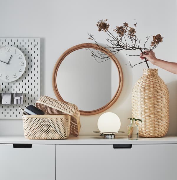 Un vase décoratif KAFFEBÖNA et une boîte SMARRA, tous deux en bambou, sur une armoire blanche.