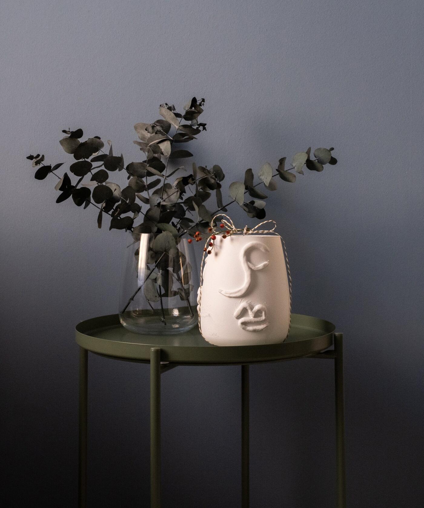 Un vase en verre avec de l'Eucalyptus et un vase en terracota sur une table d'appoint verte