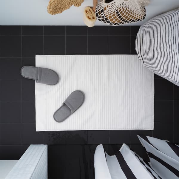 Una alfombra de baño ALSTERN de IKEA está en el sueño de un baño color negro. Hay un par de sandalias grises en la alfombra.