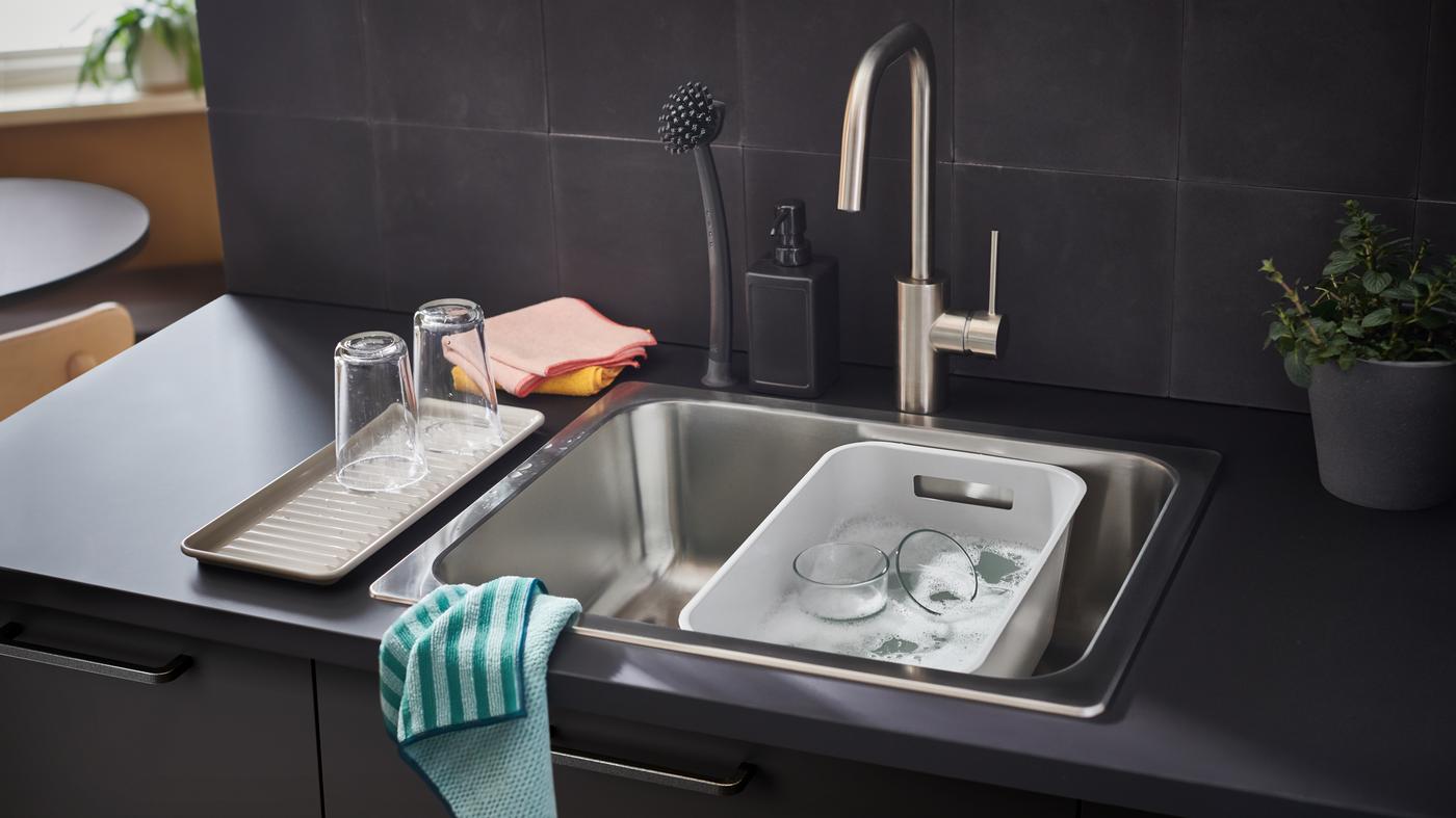 Una barra de trabajo EKBACKEN de color carbón con una tarja que contiene un contenedor GRUNDVATTNET gris, trapos de microfibra y accesorios.