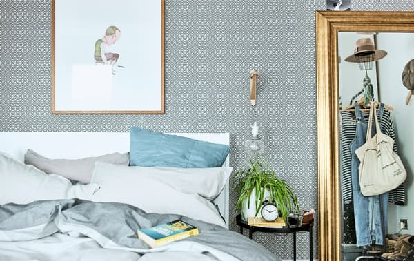 Una camera da letto con carta da parati fantasia, biancheria da letto nei toni del blu e uno specchio con cornice dorata che riflette uno stand appendiabiti - IKEA