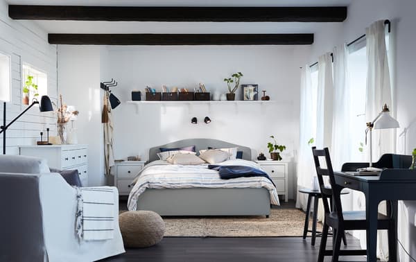 Una camera da letto dallo stile tradizionale e coordinato, con un letto HAUGA beige, una poltrona bianca e una scrivania blu scuro-verde - IKEA