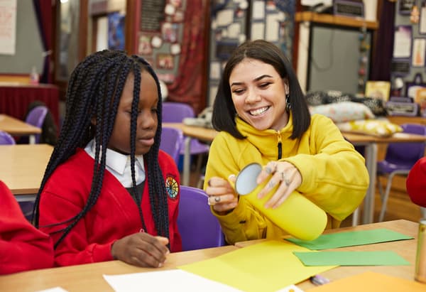 Una co-worker IKEA aiuta una bambina con l'uniforme della scuola impegnata in attività di bricolage con della carta colorata.