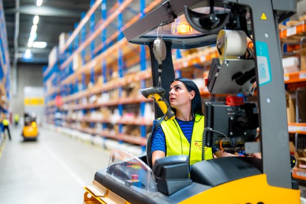 Una co-worker IKEA con lunghi capelli scuri guida un carrello elevatore nell'area self-service.